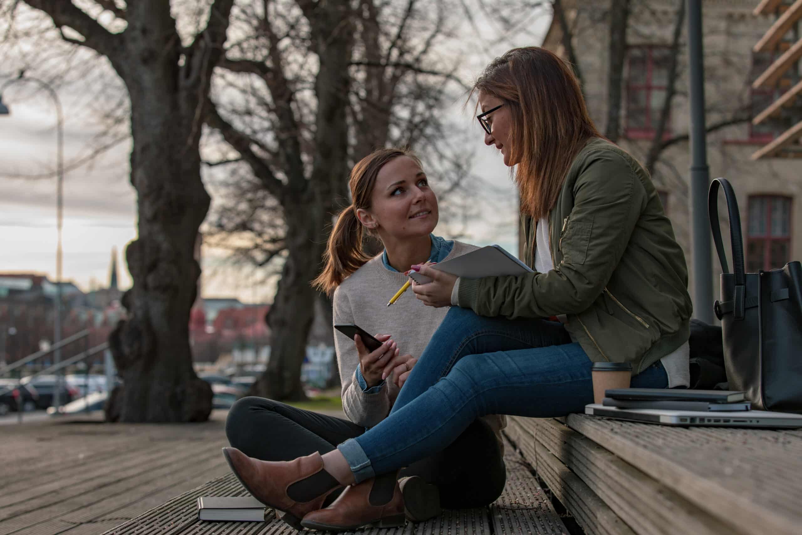 Two women studying in the city Two women are studying outdoors in Gothenburg city. One of them is reading a book and the other one is holding a notebook and a pen.