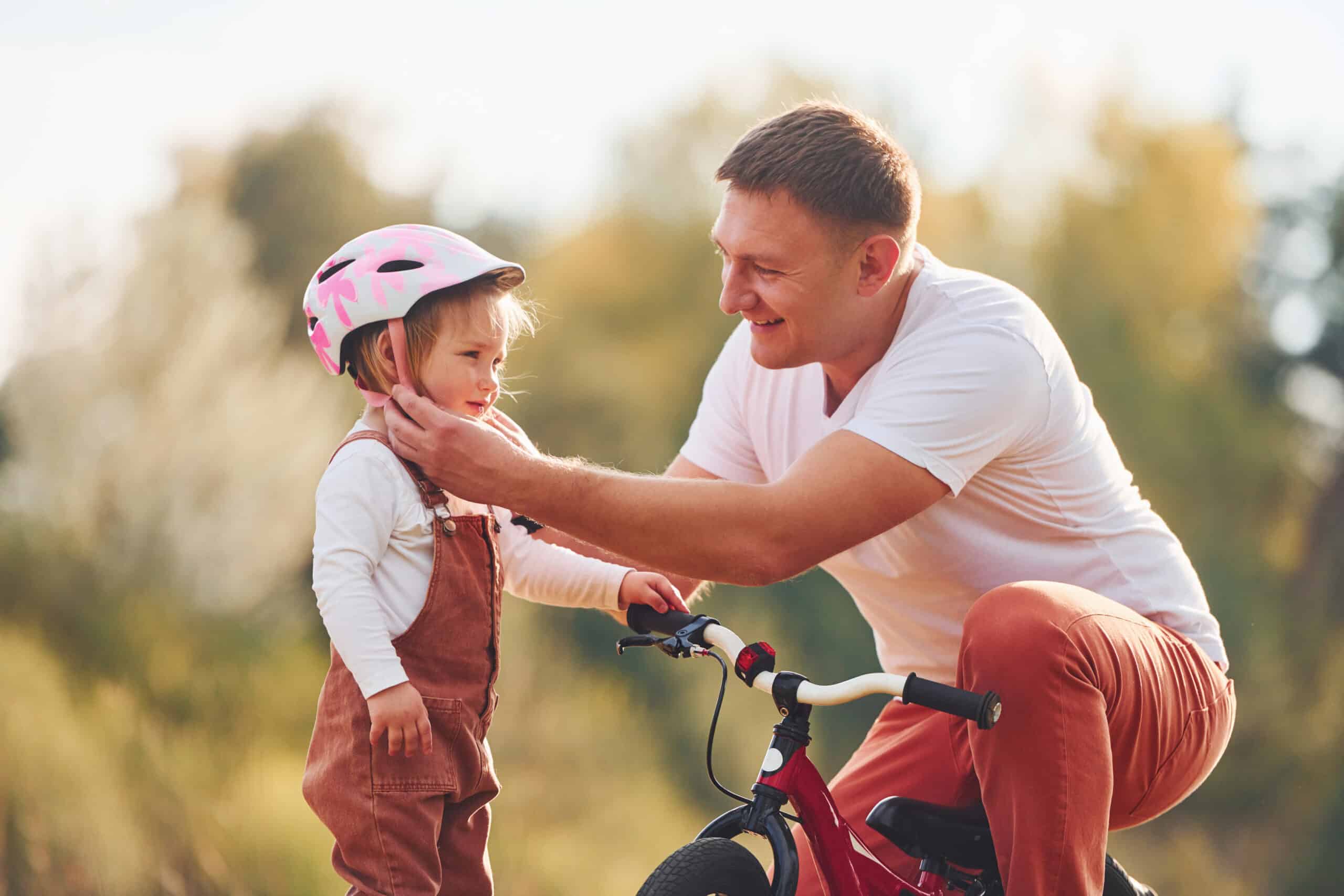 Beautiful sunlight. Father in white shirt teaching daughter how to ride bicycle outdoors Beautiful sunlight. Father in white shirt teaching daughter how to ride bicycle outdoors.
